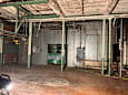 A large, empty warehouse with a green ladder and a black vehicle in the foreground.