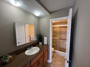 A bathroom with a sink, mirror, and a door leading to a shower.