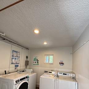 A small white washing machine is in a small room with a window.