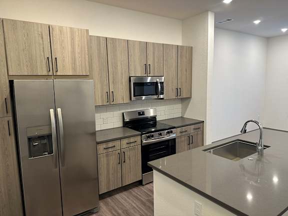 A kitchen with a refrigerator, microwave, oven, sink and cabinets.