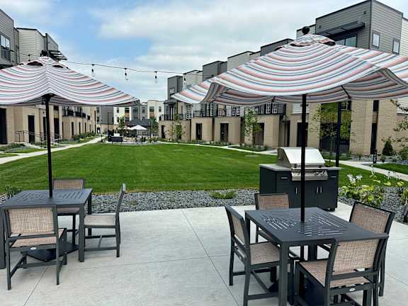 a patio with tables and umbrellas and a lawn in front of apartments at Meridian at CityPlace in Woodbury, MN 55125