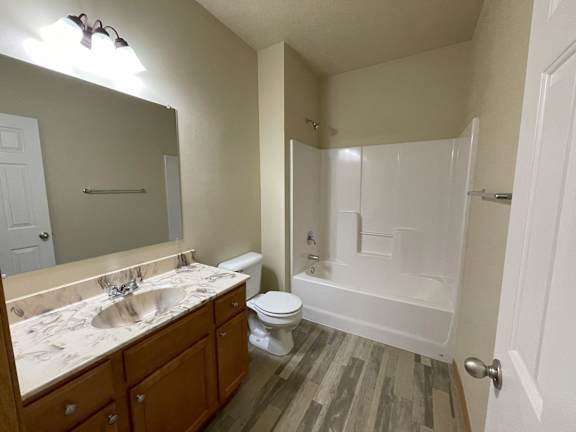 A white toilet sits in a bathroom with a wooden floor and a white shower.