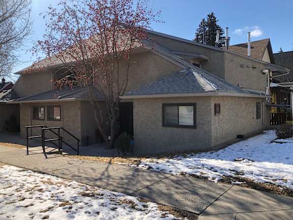 A house with a grey roof and a tree with red leaves in front.