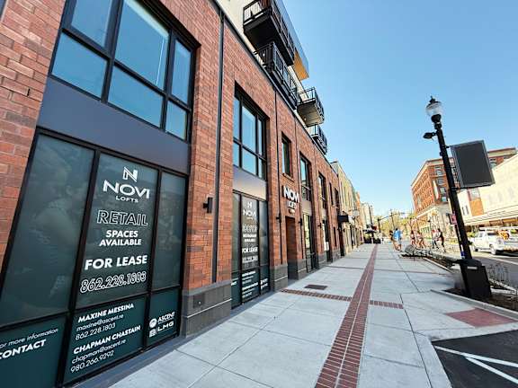 A street view of a building with a sign that says "NOVI RETAIL SPACES AVAILABLE FOR LEASE".