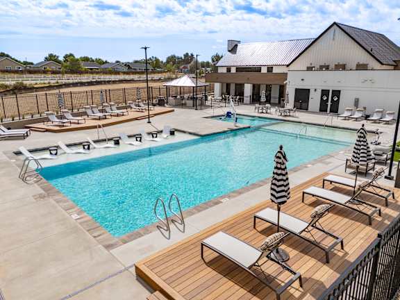 A large outdoor swimming pool with sun loungers and a striped umbrella at Alante Homes at Spring Run, Caldwell, 83607