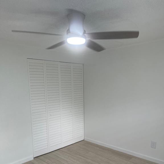 A ceiling fan with lights is mounted on a white wall above a white radiator.