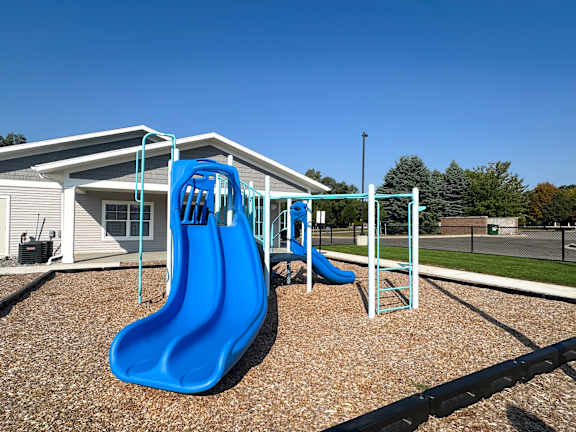 A blue slide in a playground with a house in the background.