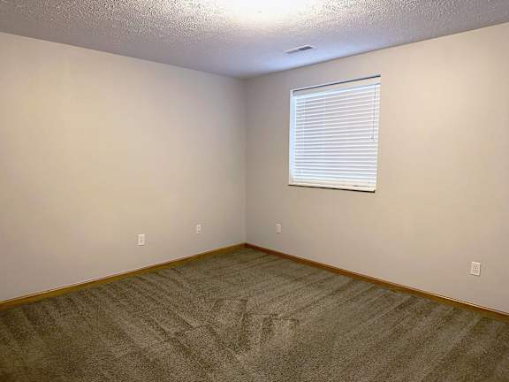 A room with a carpeted floor and a window with blinds.