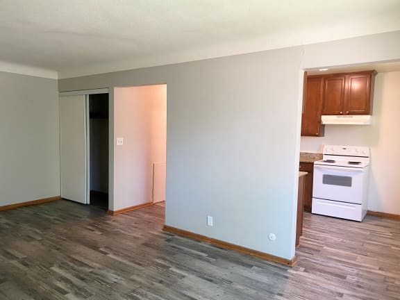 an empty living room with a kitchen in the background
