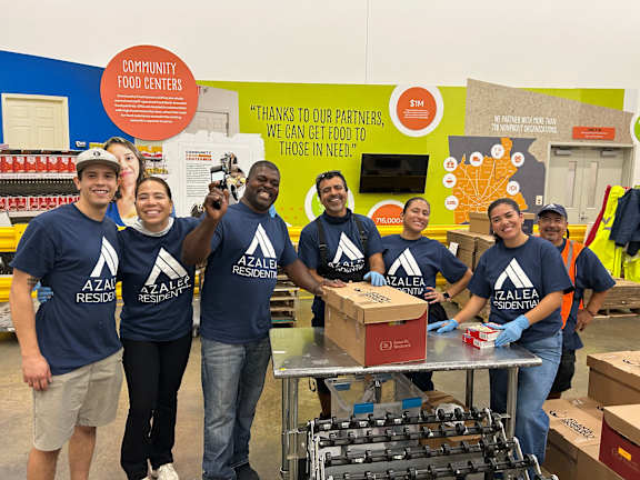 A group of people in blue shirts with the logo "AZALEA RESIDENT" are standing in front of a table with boxes on it.