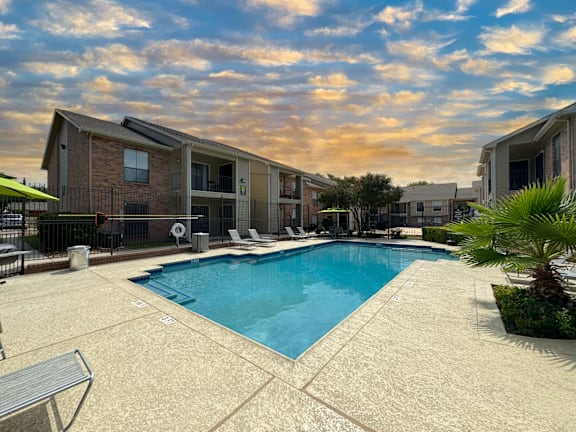 A swimming pool surrounded by a concrete patio and a building in the background.