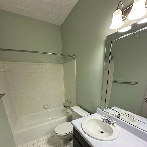 A white sink is mounted under a mirror in a tiled bathroom.