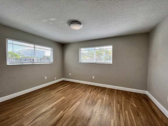 an empty living room with wood flooring and two windows  at Palm Gardens @ Biscayne Gardens, Florida