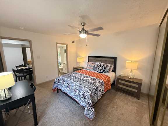 A bedroom with a bed, a ceiling fan, and a dining table.
