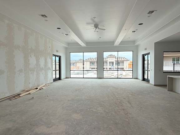 A large empty room with a ceiling fan and large windows.