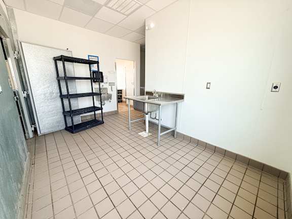 A kitchen area with a fridge, a table and a shelf.