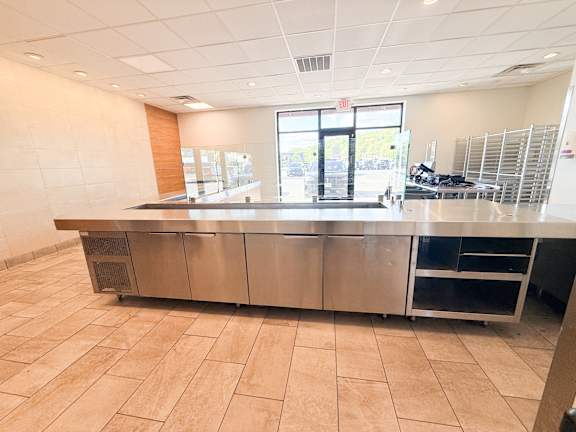 A large, empty commercial kitchen with stainless steel appliances and tiled flooring.