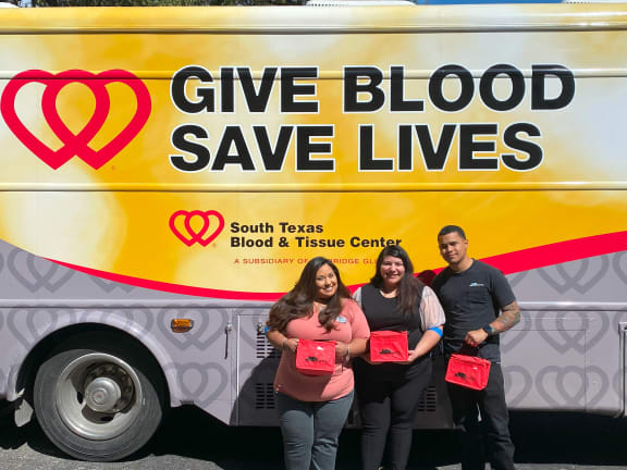 four people standing in front of a give blood save lives bus