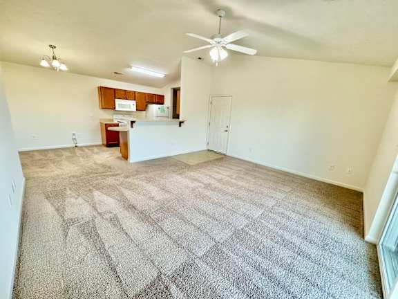 the living room and kitchen of an empty apartment with carpeting and a ceiling fan  at Hawthorne Properties in Lafayette, IN 47905