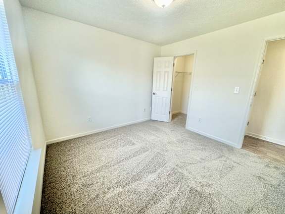 an empty living room with carpet and a door to a closet  at Hawthorne Properties in Lafayette, IN 47905
