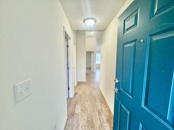 a hallway with a blue door and white walls and wood floors at Hawthorne Properties in Lafayette, IN 47905