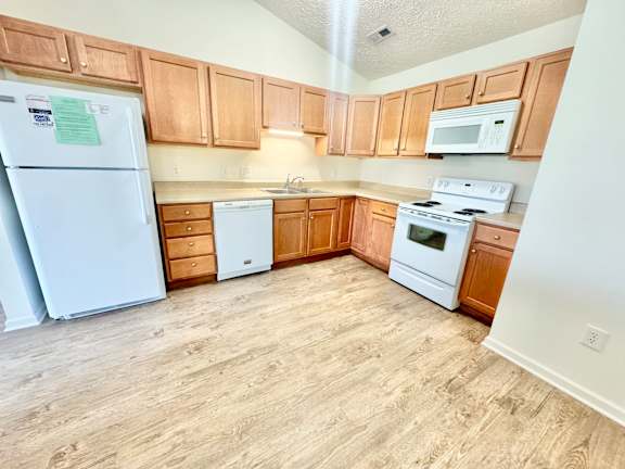 an empty kitchen with white appliances and wooden cabinets at Hawthorne Properties in Lafayette, IN 47905