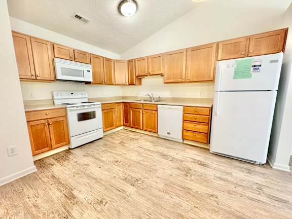 an empty kitchen with white appliances and wooden cabinets at Hawthorne Properties in Lafayette, IN 47905
