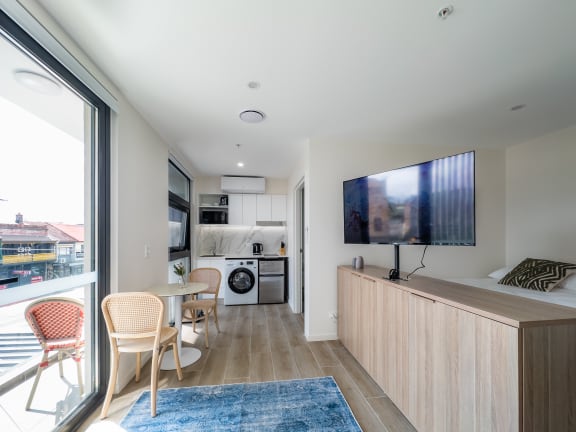 a living room with a tv and a kitchen with a table and chairs
