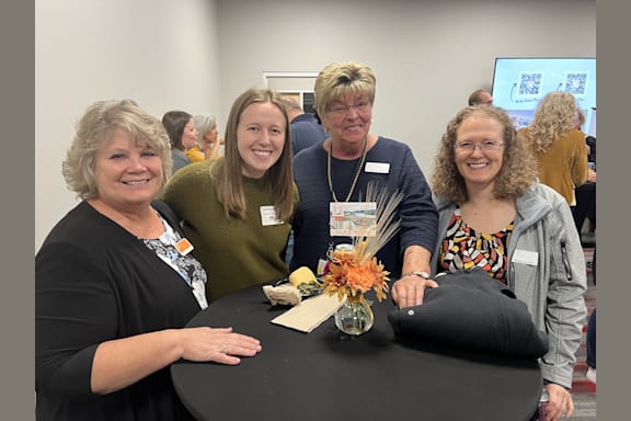 four women sitting at a table posing for a picture