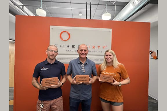 three people holding awards in front of an orange wall
