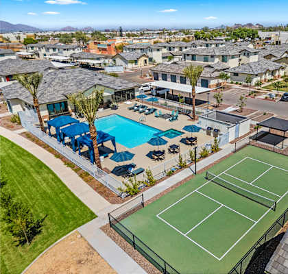A tennis court is surrounded by a pool and palm trees.