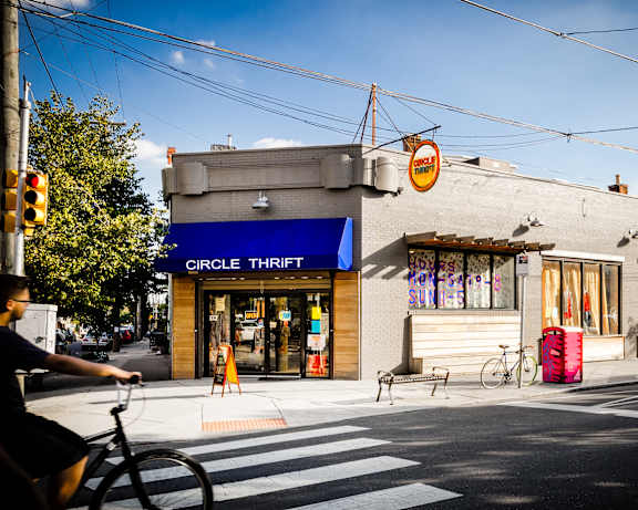 A man is riding a bicycle on a street with a Circle Thrift store in the background.