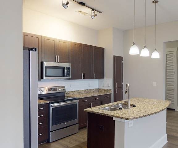 A cozy kitchen with stainless steel appliances, marble countertop with ample space, and large wooden cabinets at Lofts at Watters Creek Apartments. 