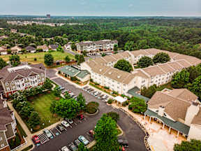 A large white building with a green roof is surrounded by trees and other buildings.
