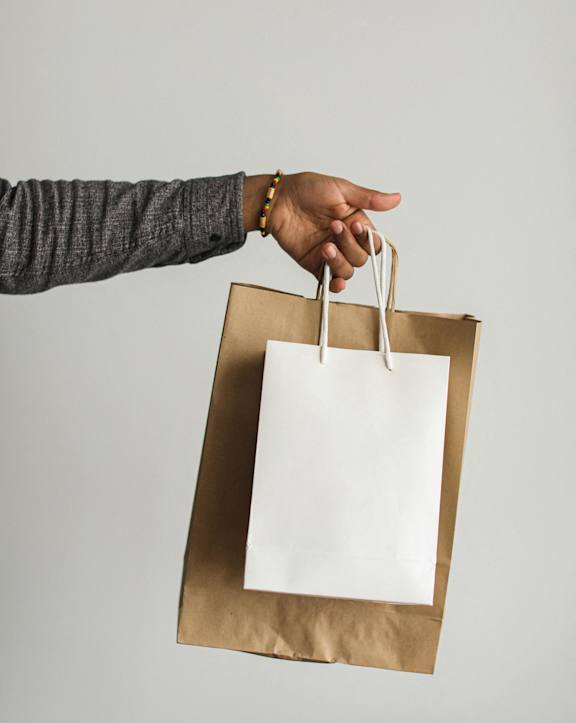 A hand holding a brown paper bag with a white interior.