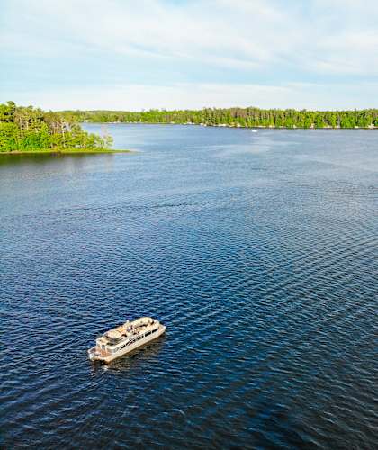 A boat is sailing on a lake with trees on the shore at The Villas at Sand Lake Resort, Sturgeon Lake, 55783