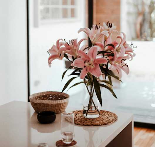 a vase of pink flowers on a table in front of a window