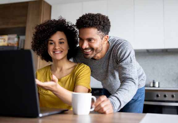 a man and woman looking at a laptop computer in a kitchen
