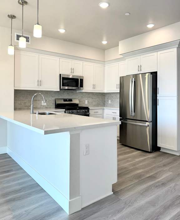 an open kitchen and living room with white cabinets and stainless steel appliances
