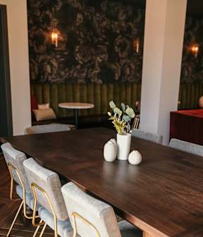 A dining table with chairs and a vase of flowers on top.