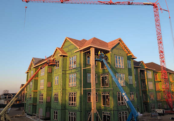 A large green building under construction with a crane in the background.