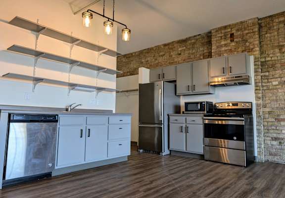 a kitchen with white cabinets and stainless steel appliances and a brick wall