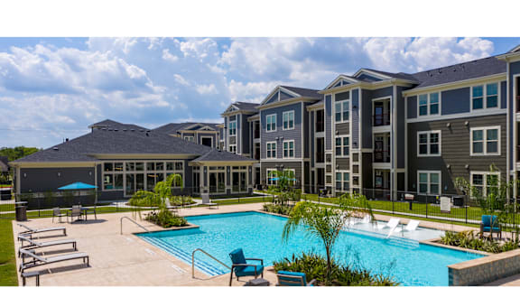 a large swimming pool with chairs around it in front of an apartment building