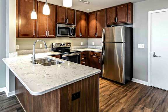Full view of the kitchen with dark wood flooring and cabinets, stainless steel appliances and white quartz countertops in a one bedroom apartment at Midtown Crossing apartments