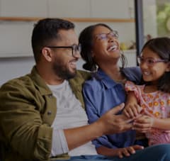 A man and a woman are sitting with a child, all are laughing.