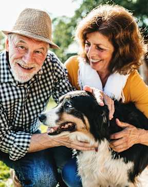 An elderly man and woman are sitting on the grass with a dog.