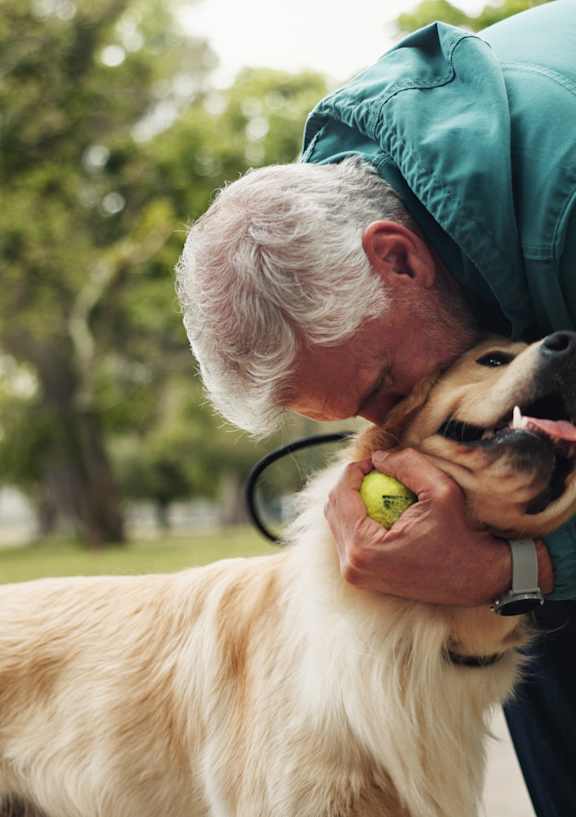 A man in a green jacket is playing with a golden retriever in a park.