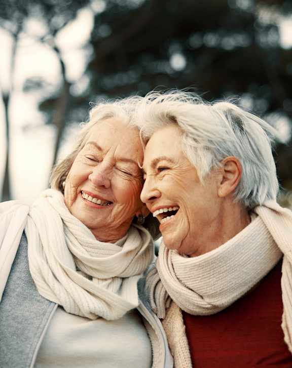 Three elderly women laughing together outdoors.