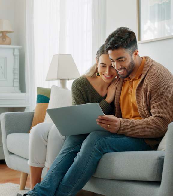 A man in a striped shirt is using a laptop on a grey couch.