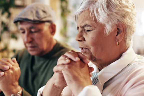 An elderly couple is praying together.